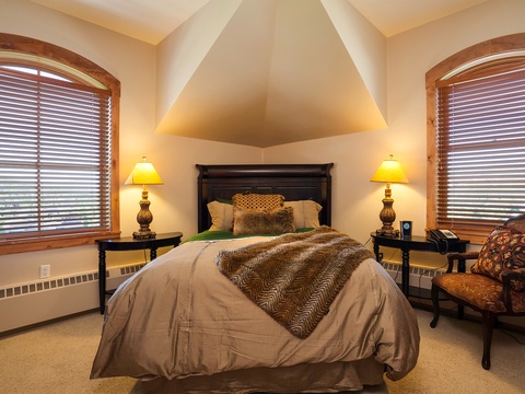 Sink into soft bedding beneath vaulted ceilings, where twin arched windows frame your view and gentle lamplight creates your cozy retreat.