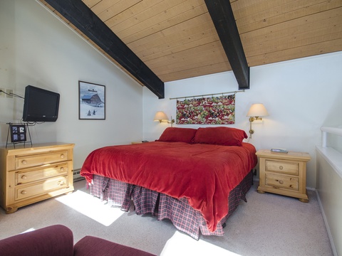 Drift off under charming exposed beams with warm bedside lamps casting a soft glow. Your cozy retreat features a plush red bedspread, mountain-inspired art, and entertainment at your fingertips.