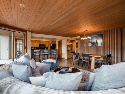 Relax in your open-concept living space, where warm wood ceilings meet modern comfort. Gather around the cozy seating, cook in your full kitchen, or share meals at the dining table surrounded by natural textures.