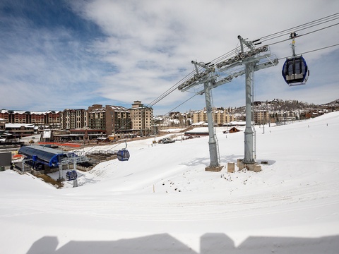 Gondola lift connecting the ski village to snowy slopes, with alpine lodges and mountain terrain in the background—a convenient gateway to winter recreation.