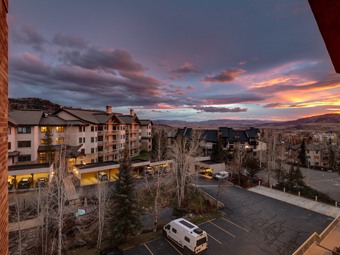 Stunning sunset over the mountain resort neighborhood, with vibrant skies painting the horizon beyond nearby lodges and parking areas.