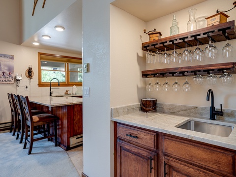 Your own stylish wet bar awaits with polished granite counters, stainless sink, and handcrafted wood shelves displaying glassware—perfect for mixing drinks after a day exploring Steamboat.