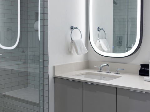 Your sleek bathroom features a modern vanity with soft-close cabinetry, premium fixtures, and fresh towels waiting for you, while the glass-enclosed shower beckons with crisp white tiles.