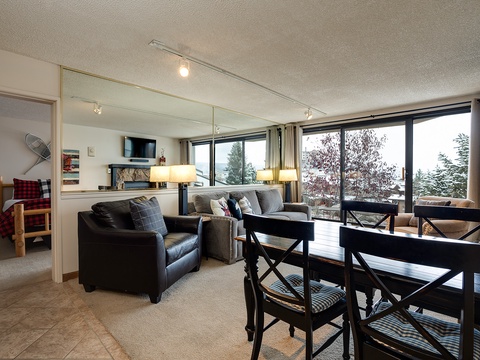 Relax in your open-concept living and dining area, where cozy seating, a warm fireplace, and stunning lake views through floor-to-ceiling windows create the perfect retreat for memorable evenings.