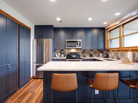 Your fully equipped kitchen features elegant navy cabinetry, marble countertops, and modern appliances, perfect for preparing meals and gathering with loved ones over morning coffee.