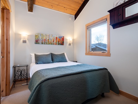 Rest easy in this serene bedroom where vaulted ceilings and warm wood accents create your peaceful mountain retreat. Wake to natural light streaming through the window, ready for your next adventure.