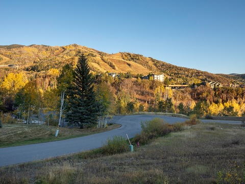 A mountain resort community nestled among vibrant autumn foliage and rolling hills, with scenic winding roads leading through the landscape beneath clear blue skies.