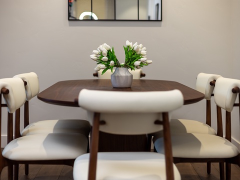 A stylish dining space with a warm walnut table and mid-century chairs, perfect for sharing meals or morning coffee together. Fresh flowers add a welcoming touch to your in-home dining experience.