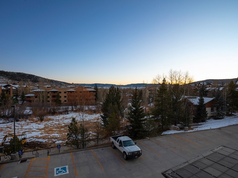 Scenic mountain village surrounded by snow-dusted hills and evergreen forests at sunset, with nearby lodging and accessible parking.