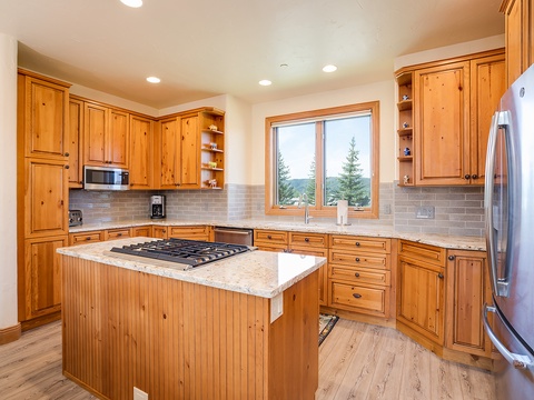 Prepare your favorite meals in this fully equipped mountain kitchen, where natural light pours in through windows showcasing serene evergreen views, and custom pine cabinetry adds rustic warmth to your stay.