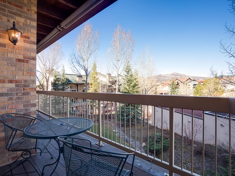 Private balcony overlooking a tranquil neighborhood with mountain views, evergreens, and seasonal trees framing the distant hills—a quiet residential setting beyond the property grounds.