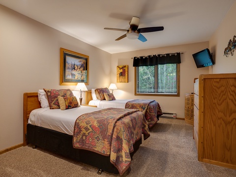 Drift off to sleep in this cozy bedroom with two comfortable beds adorned with rustic quilts, a ceiling fan keeping you cool, and a warm, lodge-inspired décor that makes you feel right at home.