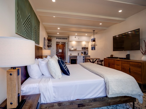 Step into your stylish studio where crisp white linens welcome you to a plush bed. Warm wood tones and modern art create a cozy retreat with a full kitchenette and entertainment for your perfect getaway.