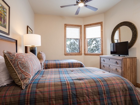 Settle into your cozy bedroom where plaid bedding and mountain views create a warm alpine retreat. The ceiling fan keeps you comfortable year-round.