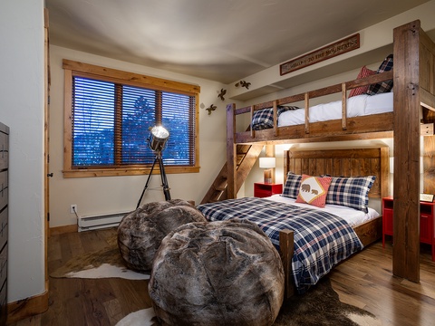 Your mountain retreat features a custom bunk room with cozy plaid bedding, rustic wooden furniture, and playful touches like plush beanbags—perfect for family bonding after a day on the slopes.