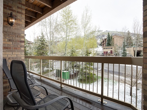 Private balcony overlooking a peaceful neighborhood with mountain views, trees transitioning to spring, and comfortable seating for relaxing mornings or evenings outdoors.