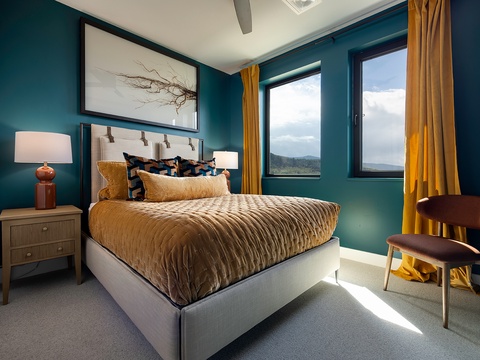 Sink into luxurious bedding beneath vibrant teal walls, where your mountain view through expansive windows brings the outdoors right to your bedside. Golden accents and natural light create a warm, inviting retreat.
