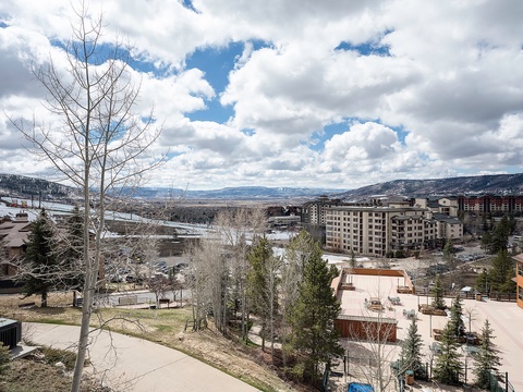 Panoramic mountain resort area featuring multi-story residential buildings nestled among evergreens and aspen trees with dramatic valley and distant peak views stretching beyond.