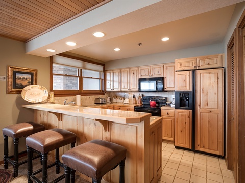 Your fully equipped kitchen features warm wood cabinetry, stainless appliances, and a breakfast bar with three stools—perfect for morning coffee or casual meals together.
