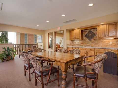 Gather around this spacious dining area where your group can share meals and stories. The rustic wood table, stone backsplash, and well-equipped kitchenette create a warm communal space for unforgettable moments.