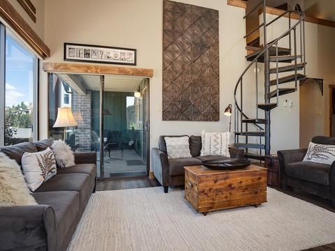 Sink into plush leather sofas beneath soaring ceilings, where a spiral staircase invites exploration and your private balcony awaits just beyond the glass doors—your stylish retreat blends rustic warmth with modern comfort.