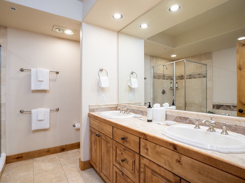 Your spacious en-suite bathroom features a glass-enclosed walk-in shower, dual vanities with ample counter space, and soft towels ready for your arrival.