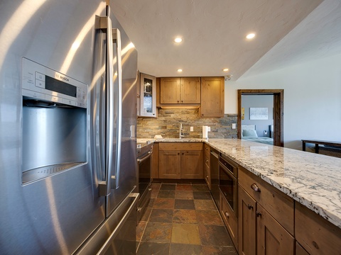 A modern kitchen awaits with gleaming granite countertops, warm wood cabinetry, stainless-steel appliances, and a rustic stone backsplash that adds character to your cooking space.