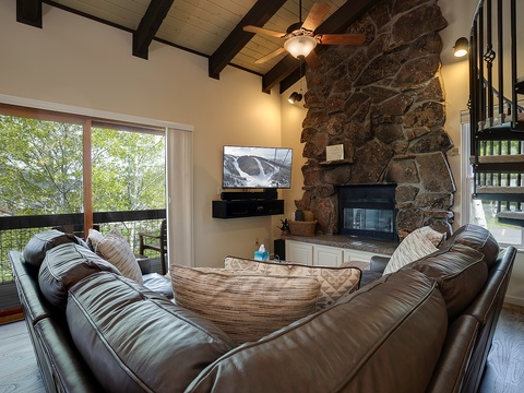 Cozy up in your spacious living room with vaulted ceilings, a striking stone fireplace, and plush leather seating. Large windows frame lush forest views, inviting natural light into your mountain retreat.