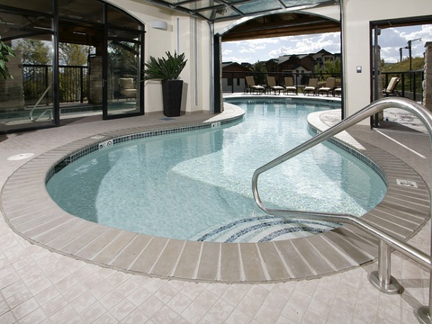 This inviting indoor-outdoor pool area flows seamlessly from the enclosed section through open archways to the sunny pool deck beyond, where lounge chairs await your relaxation under bright skies.