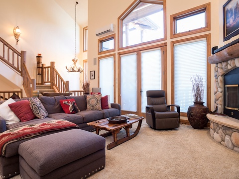 Picture yourself unwinding in this spacious living room, where sunlight pours through towering windows and a cozy stone fireplace invites you to relax with your favorite book or gather for evening conversation.