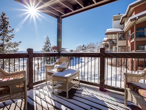 Enjoy your morning coffee on this sunny, snow-dusted balcony with cozy wicker seating and breathtaking mountain views stretching beyond the winter wonderland below.