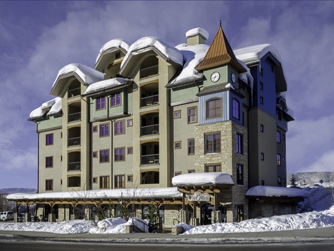 A distinctive alpine-style building with a clock tower stands proudly in a snow-covered mountain setting, marking the entrance to the property.