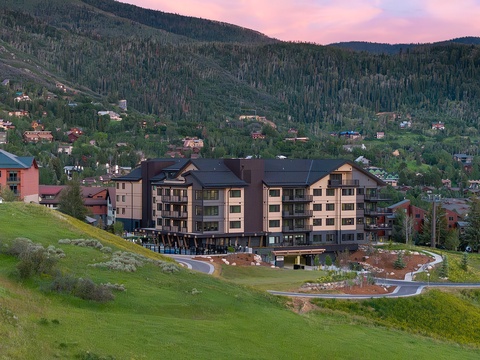 A mountain resort property nestled in a forested valley with residential buildings dotting the hillside under a soft sunset sky.