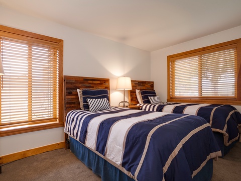 Two cozy twin beds await you in this warm bedroom, dressed in navy and white striped linens. Natural light filters through elegant wood blinds, creating a serene retreat for restful sleep.