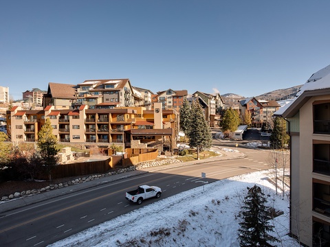 Alpine mountain village features ski lodges and multi-story resort buildings nestled among snow-dusted evergreens with mountain views beyond.