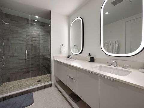 Freshen up in this sleek bathroom with a spacious walk-in shower, dual sinks, and modern backlit mirrors that create the perfect ambiance for your morning routine.