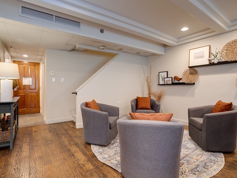 Settle into your cozy basement living space, where plush gray chairs and warm wood floors invite relaxation beneath soft lighting and thoughtful décor touches.