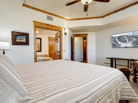 Your spacious bedroom blends mountain charm with modern comfort. Sink into the plush bed after a day exploring nearby slopes, relax beneath the ceiling fan's gentle breeze, and enjoy ski resort views on the flatscreen.