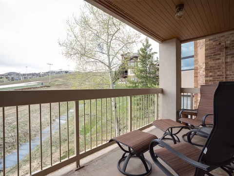 A covered balcony framed by wood ceilings overlooks a landscaped neighborhood and distant hills, offering an outdoor retreat for relaxation.