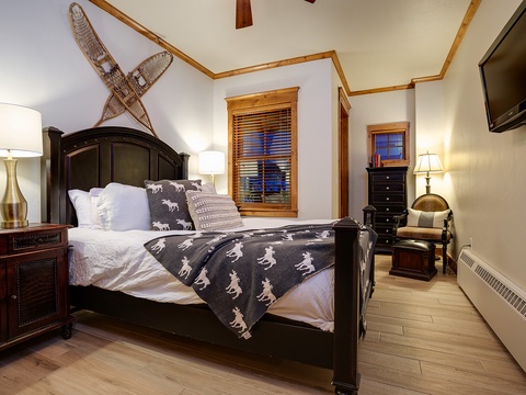 Unwind in your cozy bedroom featuring a plush bed dressed in rustic wildlife linens, vintage snowshoes above, warm wood accents, and soft lighting that invites restful nights after mountain adventures.