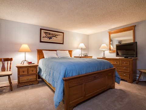 Your spacious bedroom features a cozy king bed with a rich blue comforter, warm wooden furnishings, and soft lighting to help you unwind after a day of adventure.