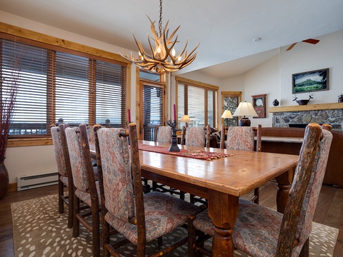Gather around this handcrafted dining table under a stunning antler chandelier. Large windows frame mountain views, while the stone fireplace adds warmth to your group meals and memorable evenings together.