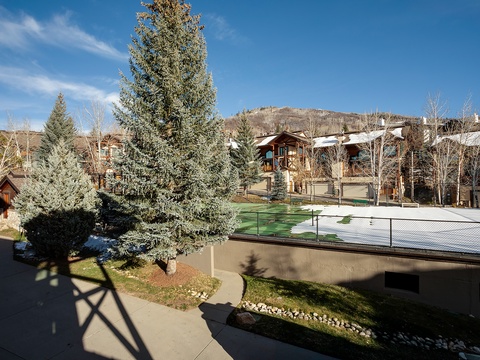 A mountain resort neighborhood framed by evergreens and open skies, with tennis courts and landscaped grounds marking the arrival area.