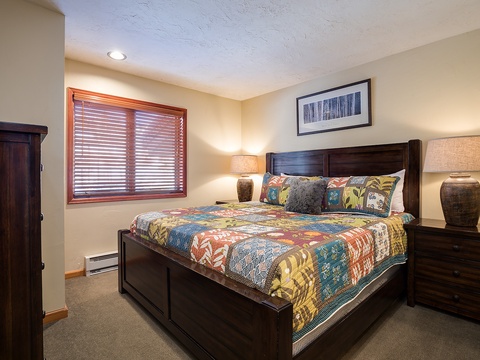 Slip into this cozy bedroom with a plush king bed dressed in colorful quilts and soft pillows. Natural light filters through wooden blinds, while warm lamps on each nightstand create a peaceful retreat after your day of adventure.