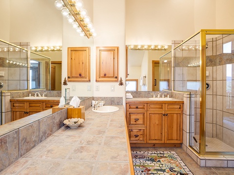 Unwind in your spacious master bath with dual vanities, elegant stone counters, a glass-enclosed shower, and warm wood cabinetry—all beautifully lit for your comfort.