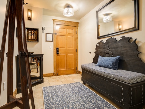 Step into your welcoming entryway featuring unique handcrafted furnishings and warm lighting. Store your skis on the custom rack after a day on the slopes, then sink into the cozy bench beneath a striking carved headboard.