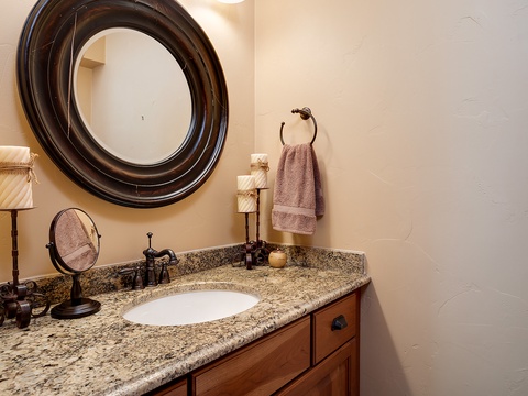 A beautifully appointed bathroom awaits, featuring elegant granite countertops, oil-rubbed bronze fixtures, and a striking circular mirror that adds timeless character to your retreat.