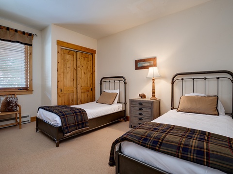 Two cozy twin beds with plaid throws invite restful nights. Soft lighting and warm wood details create a comfortable retreat where your group can unwind.
