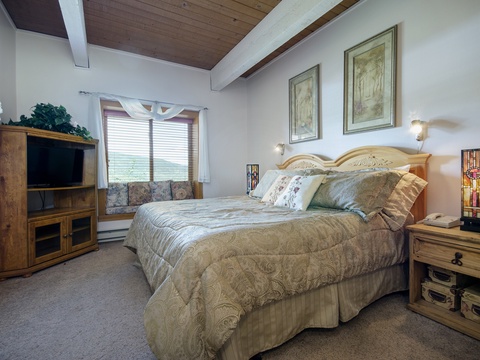 Unwind in your serene bedroom with vaulted wood ceilings, a plush king bed, and soft natural light from the window seat—your perfect mountain retreat awaits.