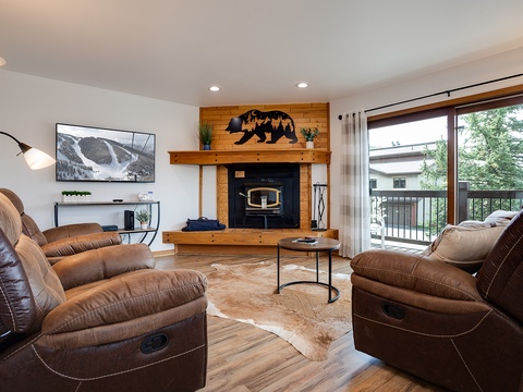 Sink into plush recliners facing your wood-burning fireplace. The space flows to a private balcony framed by forest views—perfect for unwinding after mountain adventures.